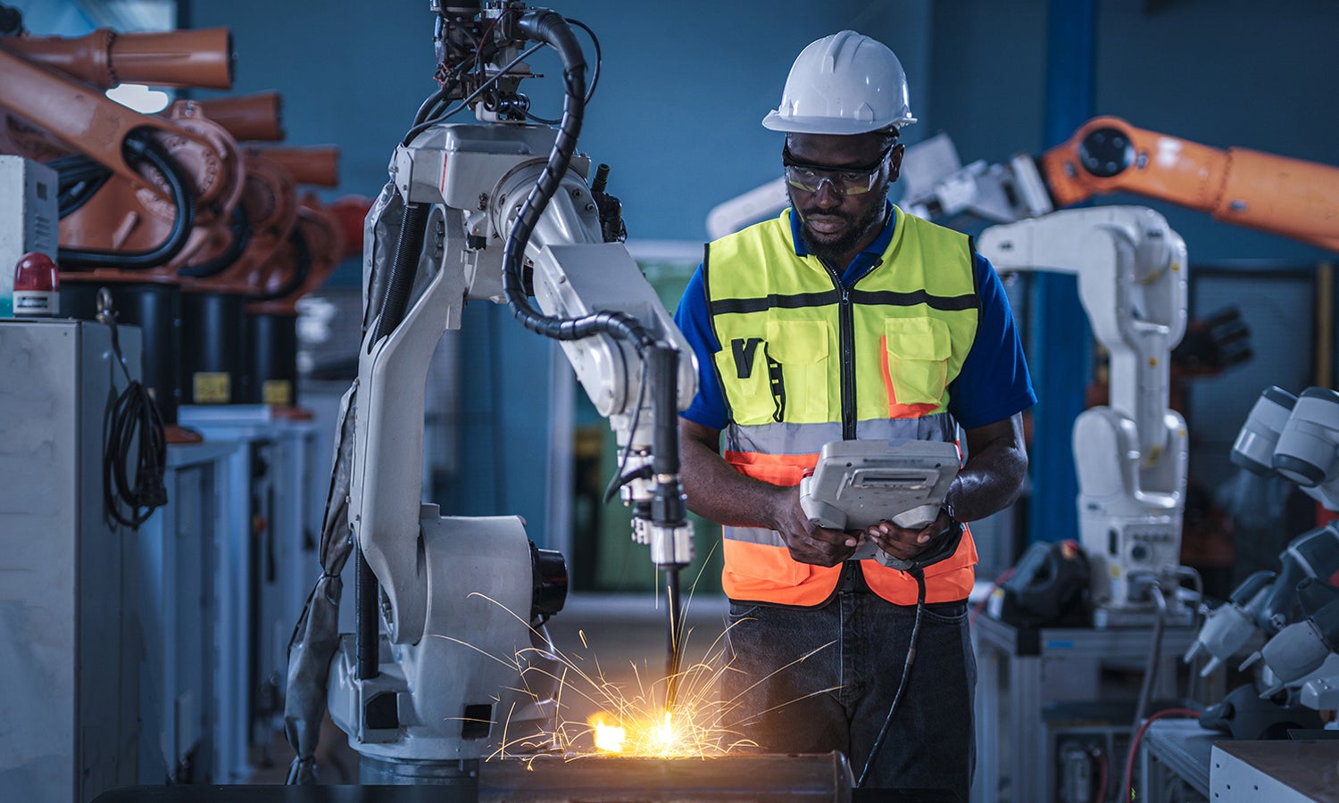 Engineers in safety equipment controlling a welding robotic arm
